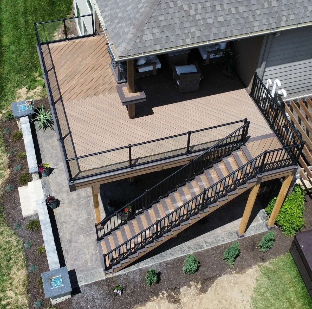 Aerial view of a deck with diagonal boards, black railings, and stairs beside a covered seating area
