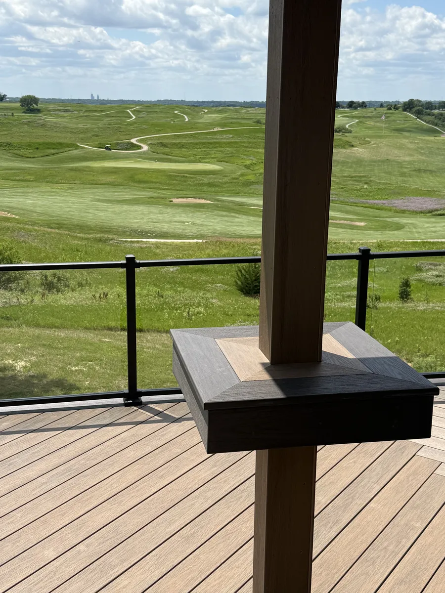 Black railing and a square post on a deck overlooking a grassy landscape