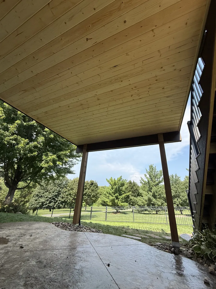 View from below a covered deck with wood plank ceiling and support posts